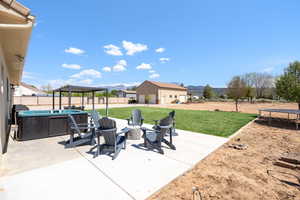 Fenced backyard with a trampoline, a patio area, a fire pit, a mountain view, and an outbuilding