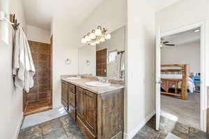 Ensuite bathroom with stone tile flooring, double vanity, a walk in shower, and a ceiling fan
