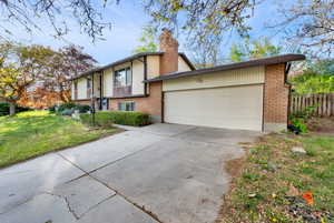 Raised ranch with brick siding, concrete driveway, a chimney, and a garage