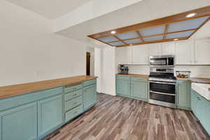 Kitchen featuring butcher block countertops, two tone cabinets, stainless steel appliances, recessed lighting, and light wood-type flooring