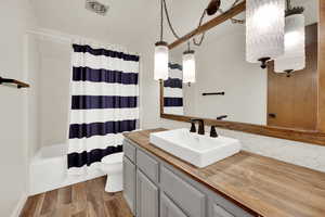 Full bathroom featuring vanity, shower / bathtub combination with curtain, dark wood-type flooring, and backsplash