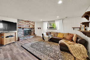 Living room with a textured ceiling, light wood-style floors, a fireplace, recessed lighting, and wooden walls