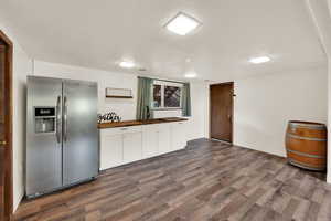 Kitchen featuring wooden counters, stainless steel fridge, dark wood-style flooring, a textured ceiling, and white cabinetry