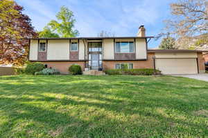 Split foyer home featuring brick siding, an attached garage, a front lawn, concrete driveway, and a chimney