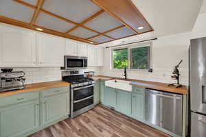 Dual tone kitchen with butcher block counters, stainless steel appliances, tasteful backsplash, light wood finished floors, and dual tone cabinetry