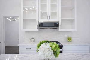 Kitchen featuring glass insert cabinets, stainless steel microwave, quartz counters, white cabinetry, and range with gas stovetop