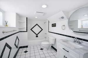 ADU bathroom with tile walls, a wainscoted wall, vanity, light tile patterned floors, and tub / shower combination