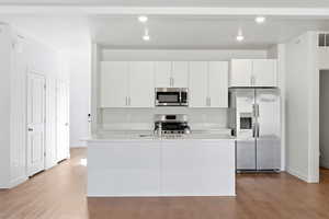 Kitchen featuring stainless steel appliances, white cabinetry, light wood-style flooring, a kitchen island with sink, and light stone countertops