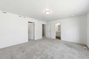 Unfurnished bedroom with carpet, ensuite bathroom, and a textured ceiling