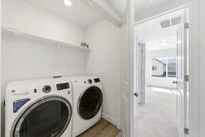 Laundry area with washer and clothes dryer, light colored carpet, and light wood finished floors