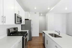 Kitchen with stainless steel appliances, white cabinets, dark wood-type flooring, recessed lighting, and light stone counters