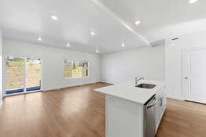 Kitchen featuring an island with sink, open floor plan, white cabinetry, light wood-style floors, and light stone counters