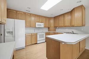 Kitchen featuring light countertops, white appliances, a peninsula, light wood finished floors, and a skylight