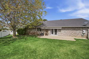 Rear view of property featuring brick siding, roof with shingles, a patio, a fenced backyard, and french doors