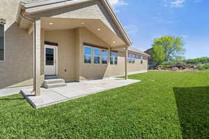 Rear view of property featuring a lawn, stucco siding, a patio area, and entry steps