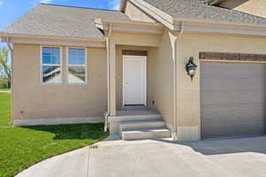 Entrance to property with a shingled roof, a garage, stucco siding, a yard, and concrete driveway
