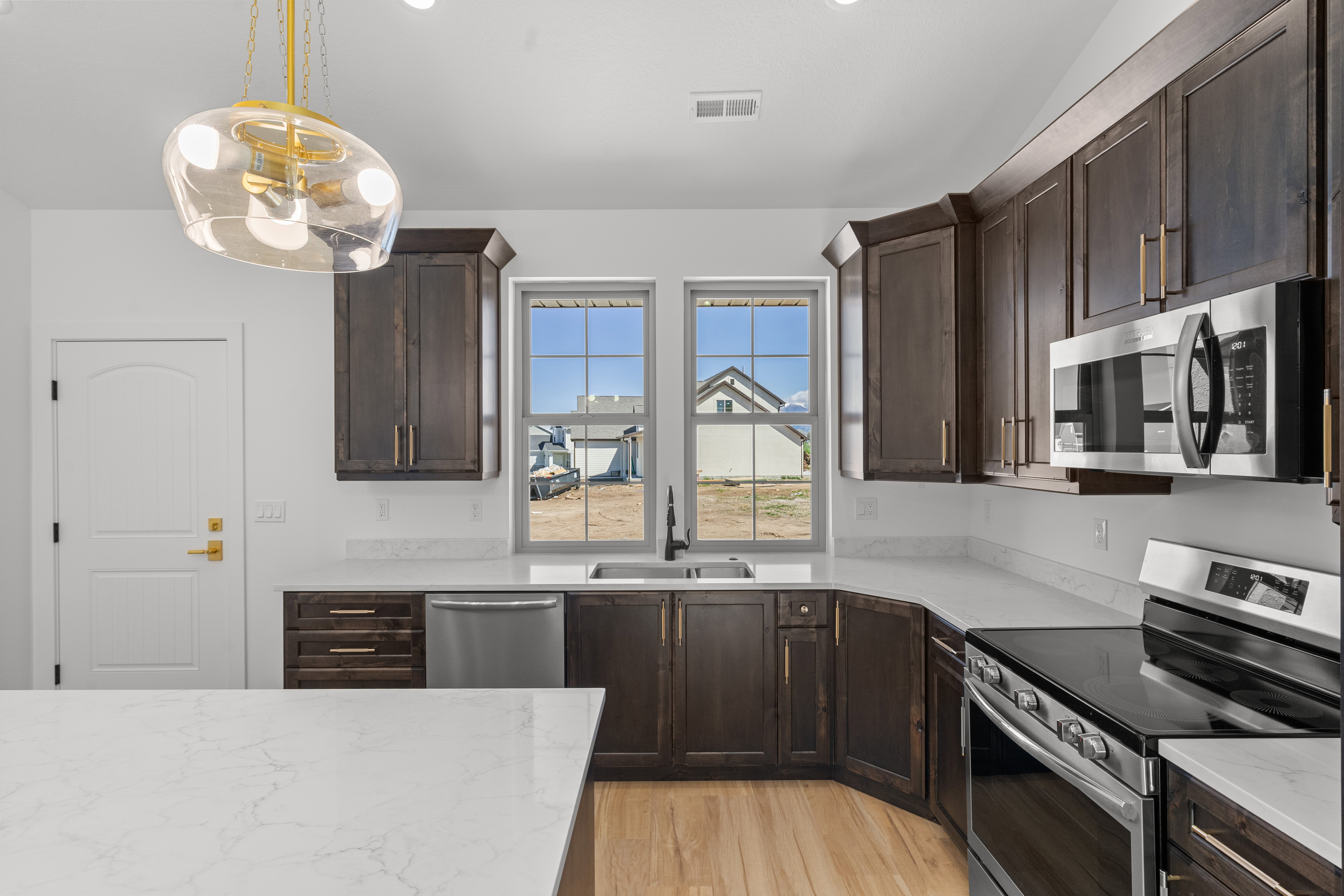 Kitchen featuring dark wood finish cabinets, stainless steel appliances, light wood finished floors, pendant lighting, and light stone counters