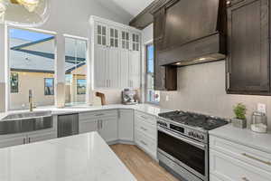 Kitchen featuring stainless steel range with gas cooktop, light stone counters, white cabinetry, tasteful backsplash, and lofted ceiling