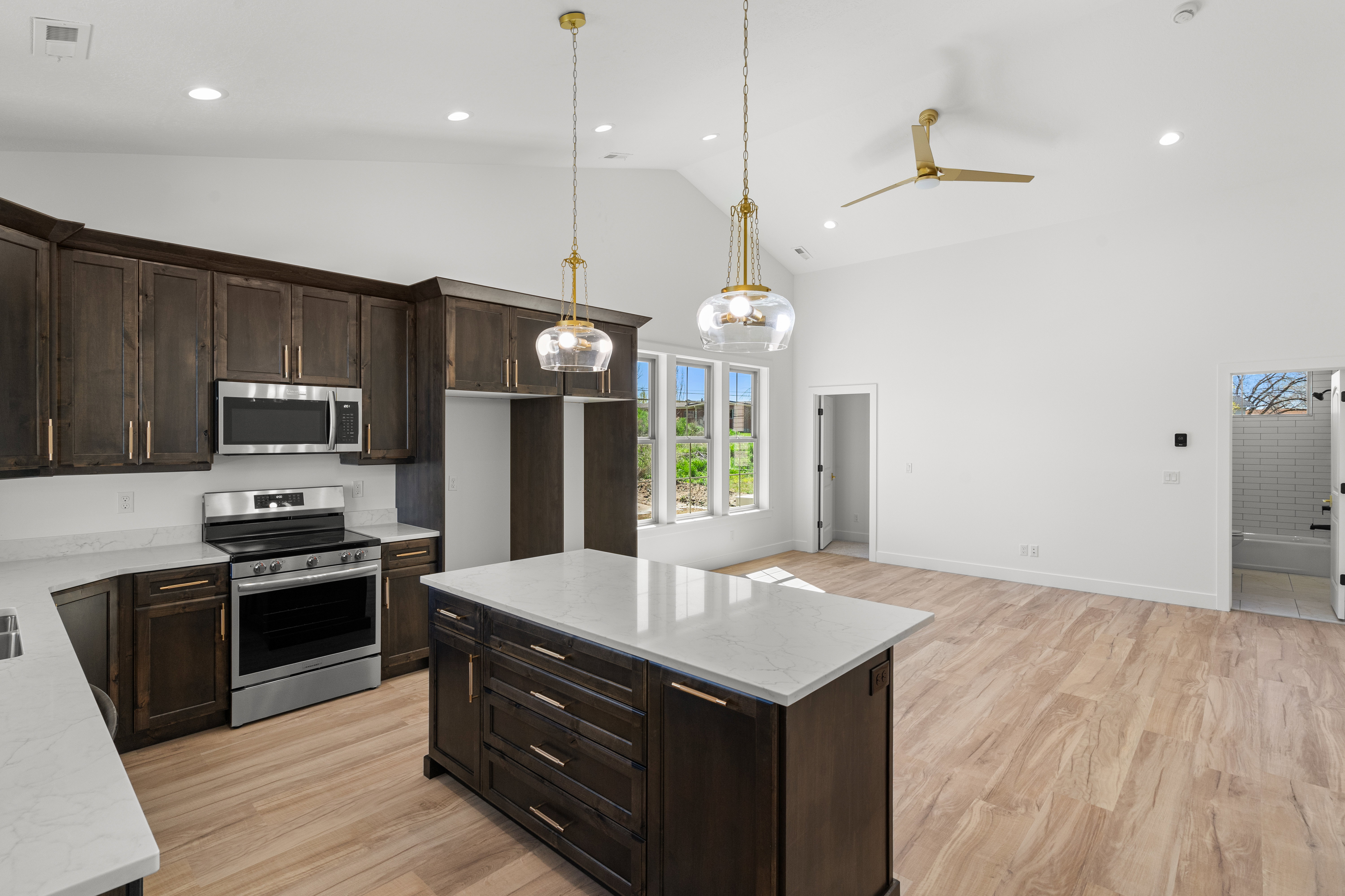 Kitchen with dark wood finish cabinetry, stainless steel appliances, light wood-type flooring, light stone countertops, and vaulted ceiling