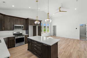 Kitchen with dark wood finish cabinetry, stainless steel appliances, light wood-type flooring, light stone countertops, and vaulted ceiling