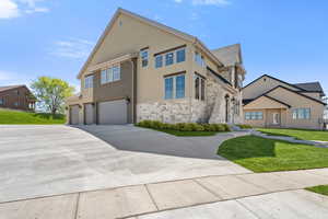 View of front of property with stone siding, a front yard, a garage, concrete driveway, and stucco siding