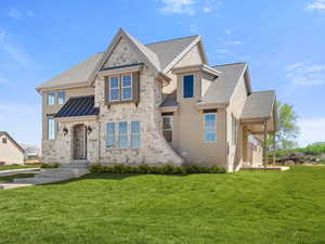 View of front of home with a standing seam roof, a front lawn, roof with shingles, and stone siding