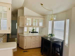 Kitchen with light countertops, light wood-type flooring, a peninsula, suspended lighting, and glass fronted cabinets