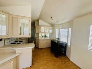 Kitchen with light countertops, glass insert cabinets, a peninsula, vaulted ceiling, and light wood finished floors