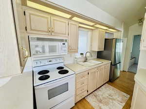 Kitchen with white appliances, light countertops, light wood finish cabinetry, light wood-type flooring, and lofted ceiling