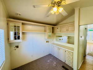 Laundry area with ceiling fan, vaulted ceiling, and dark colored carpet