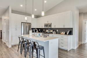 Kitchen featuring stainless steel appliances, lofted ceiling, a kitchen breakfast bar, white cabinetry, and a center island with sink