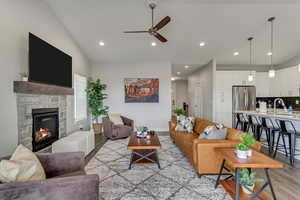 Living area with light wood finished floors, a ceiling fan, a stone fireplace, vaulted ceiling, and recessed lighting