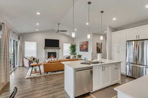 Kitchen with open floor plan, stainless steel appliances, white cabinetry, light wood-type flooring, and vaulted ceiling