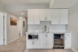 Bar with beverage cooler, white cabinets, stainless steel microwave, recessed lighting, and light stone countertops