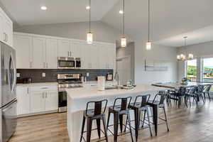 Kitchen featuring stainless steel appliances, vaulted ceiling, white cabinets, a kitchen breakfast bar, and light wood-type flooring