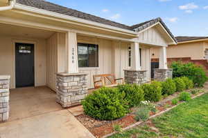 View of exterior entry featuring board and batten siding, covered porch, and stone siding