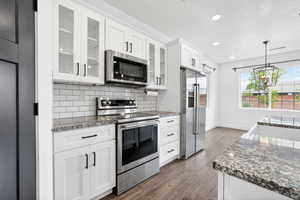Kitchen with dark stone counters, stainless steel appliances, white cabinets, and dark wood-style flooring