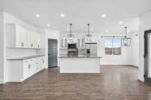 Kitchen featuring dark stone countertops, stainless steel appliances, a kitchen island with sink, and hanging light fixtures