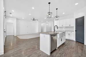 Kitchen featuring white cabinets, a ceiling fan, an island with sink, dishwasher, and backsplash