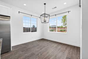 Unfurnished dining area with dark wood-style floors and hanging lights