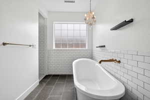 Bathroom with tile walls, dark tile patterned floors, a freestanding bath, a chandelier, and a wainscoted wall