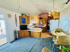 Kitchen with plenty of natural light, white appliances, a peninsula, light countertops, and vaulted ceiling