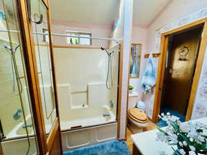 Bathroom featuring wallpapered walls, combined bath / shower with glass door, and vanity