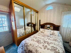 Bedroom with wallpapered walls, a closet, vaulted ceiling, and dark carpet