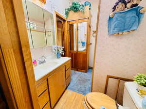 Bathroom with wallpapered walls, vanity, and light wood-style flooring