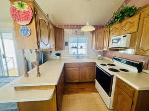 Kitchen featuring white appliances, a textured ceiling, wallpapered walls, light countertops, and wood finish cabinetry