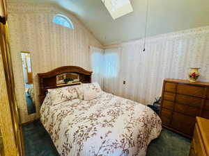 Bedroom featuring vaulted ceiling, wallpapered walls, a skylight, and dark colored carpet