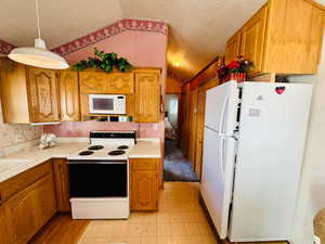 Kitchen with white appliances, light countertops, wood finish cabinetry, and light flooring