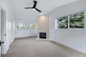 Unfurnished living room with vaulted ceiling, a ceiling fan, light carpet, a fireplace, and recessed lighting