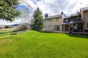 Back of house featuring a deck, a chimney, and a lawn